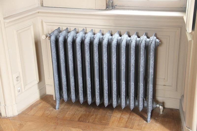 Een gietijzeren radiator onder een raam in een kamer met lambrisering