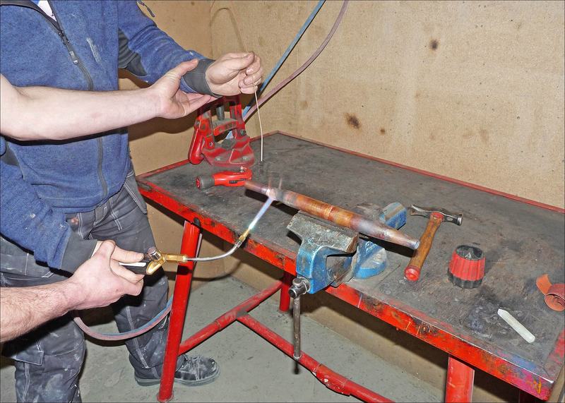 Een vakman soldeert met een brander een koperen buis op een werkbank